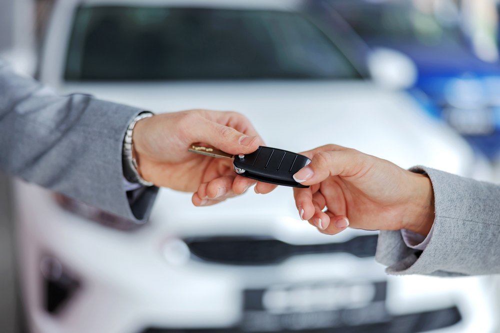 Zwei Personen übergeben sich einen Autoschlüssel vor einem weißen Auto.